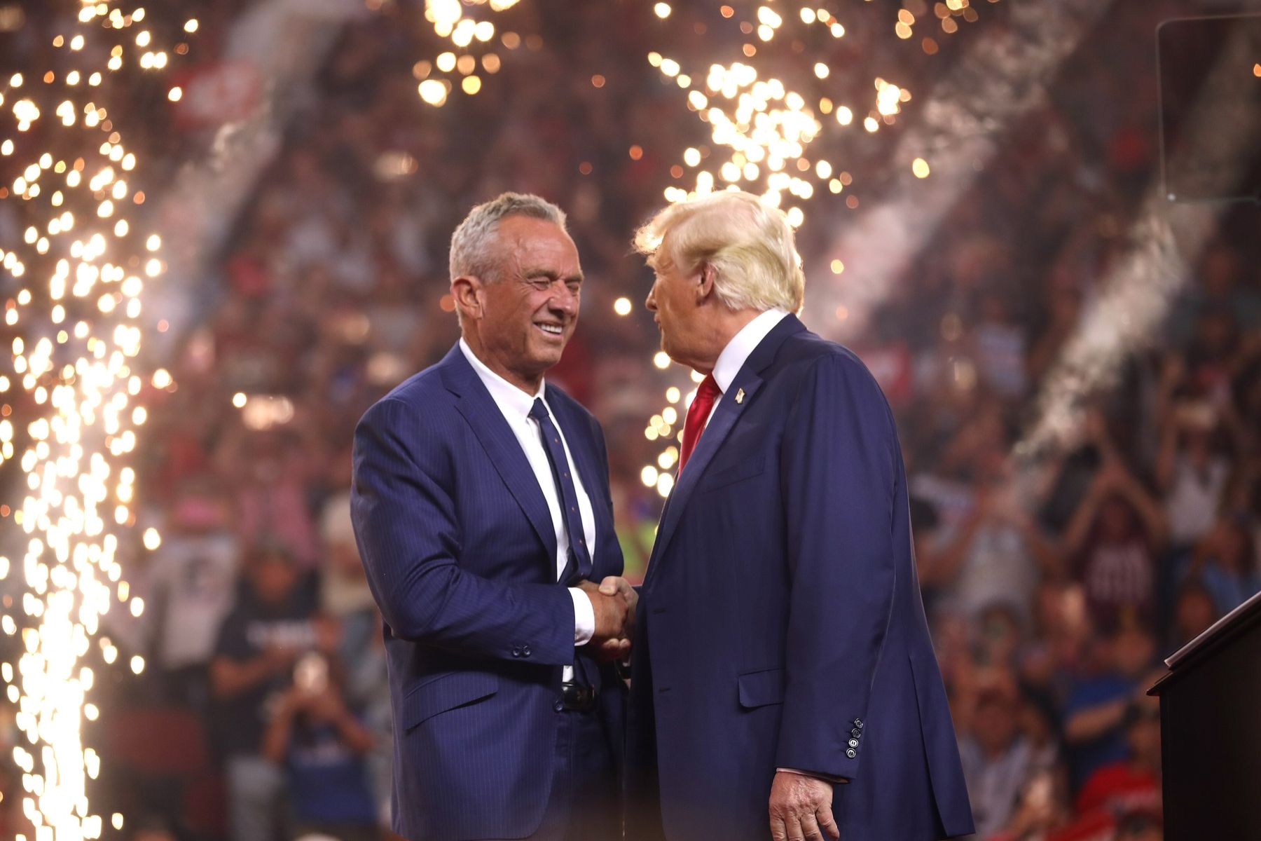 Donald Trump and Robert F. Kennedy Jr. shake hands on stage as fountains of sparks go up behind them