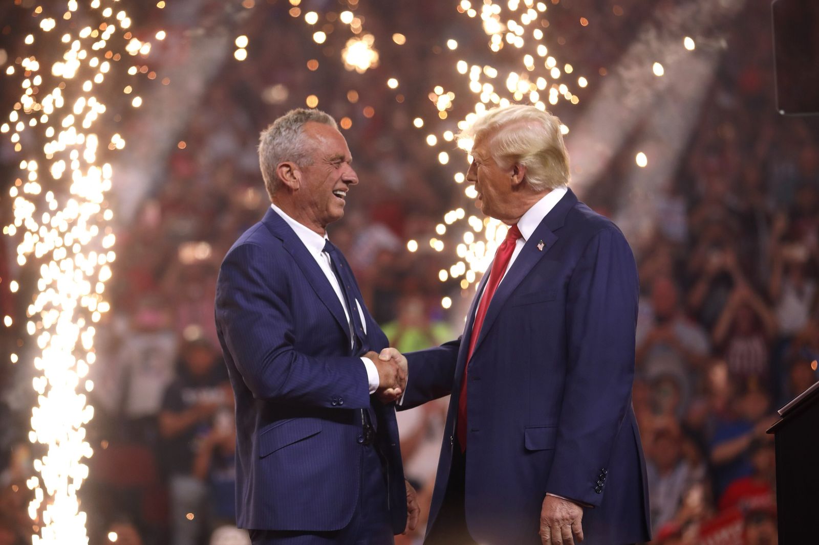 Donald Trump and Robert F. Kennedy Jr. shake hands on stage as sparks rain down behind them
