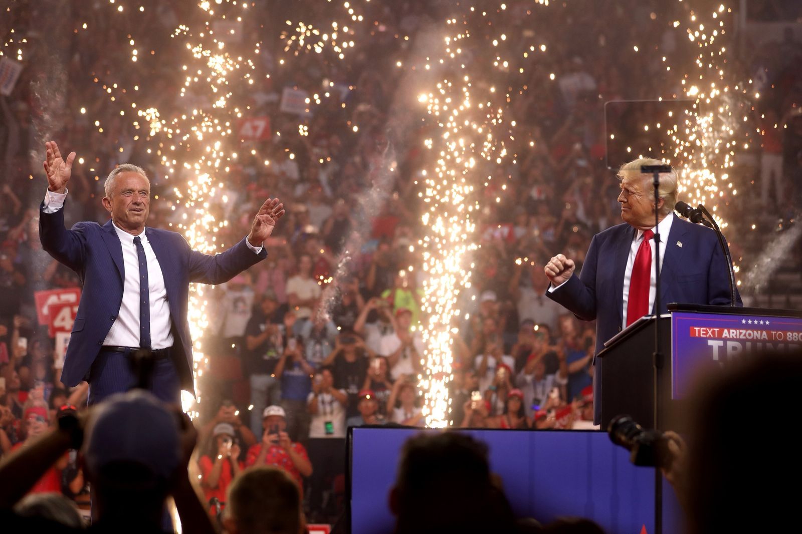 Robert F. Kennedy Jr. waves to the crowd beside Donald Trump as fountains of sparks go up